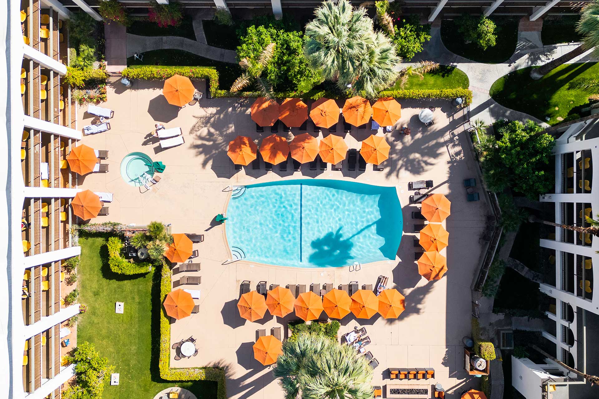 Aerial view of a resort pool area with bright orange umbrellas, lounge chairs, and surrounding greenery.