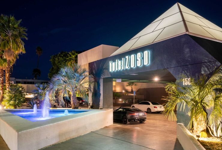 Night exterior of Hotel Zoso with a pyramid roof, illuminated sign, palm trees, and a lit fountain in the foreground.