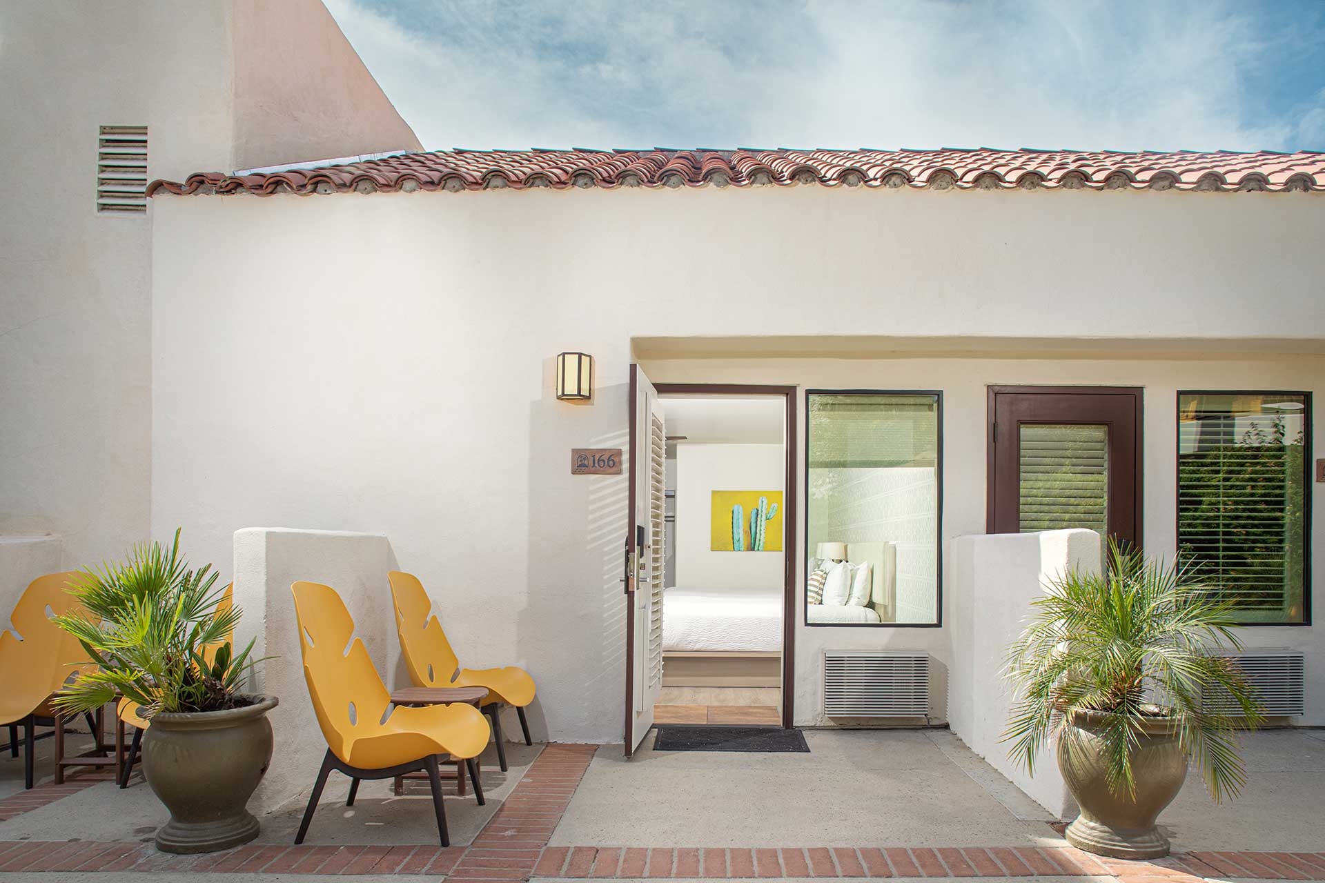 Outdoor seating area in front of a modern white house with orange chairs and large potted plants.