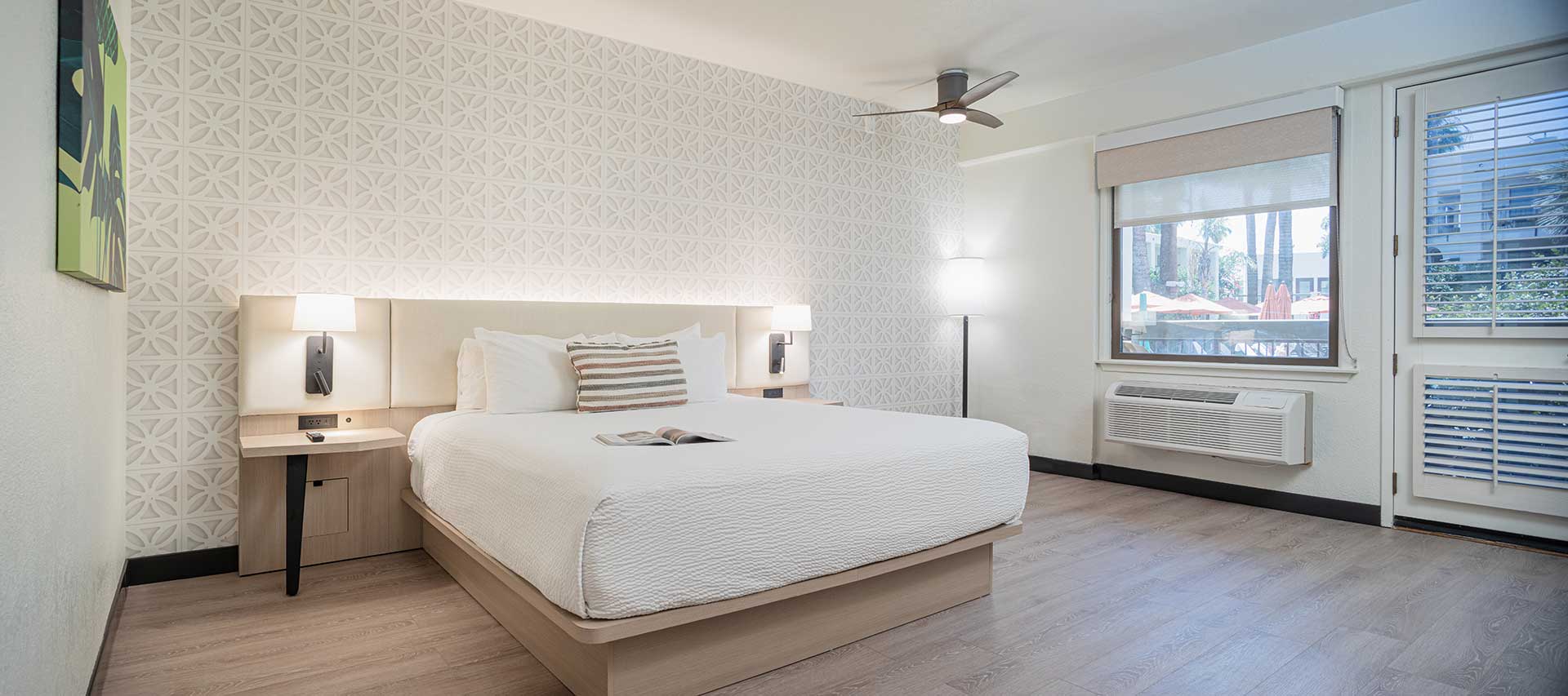 Hotel room with a large bed, white bedding, and patterned accent wall flanked by two nightstands and lamps